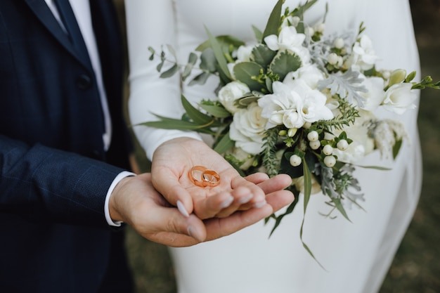 Бесплатное фото Обручальные кольца в руках жениха и невесты и с красивым свадебным букетом из зелени и белых цветов